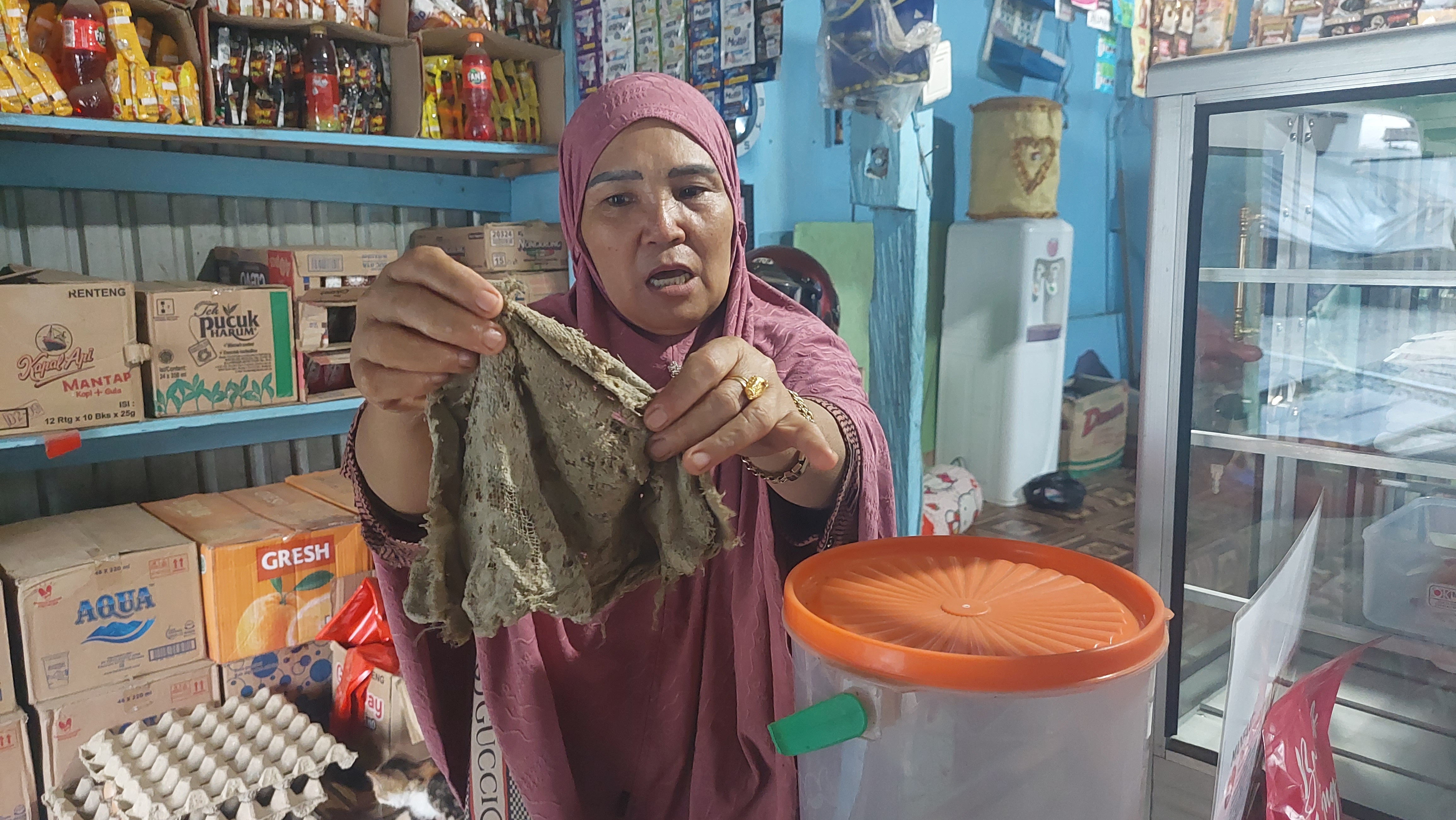 Raniah, warga Desa Bumi Harapan, Kecamatan Sepaku, Penajam Paser Utara menunjukkan kain lap yang saban hari ia gunakan untuk membersihkan barang dagangan, meja, dan etalase di tokonya dari paparan debu. Karena terlalu sering digunakan, kain tersebut sampai terkoyak. (Fitri Wahyuningsih/Kaltimtoday.co)